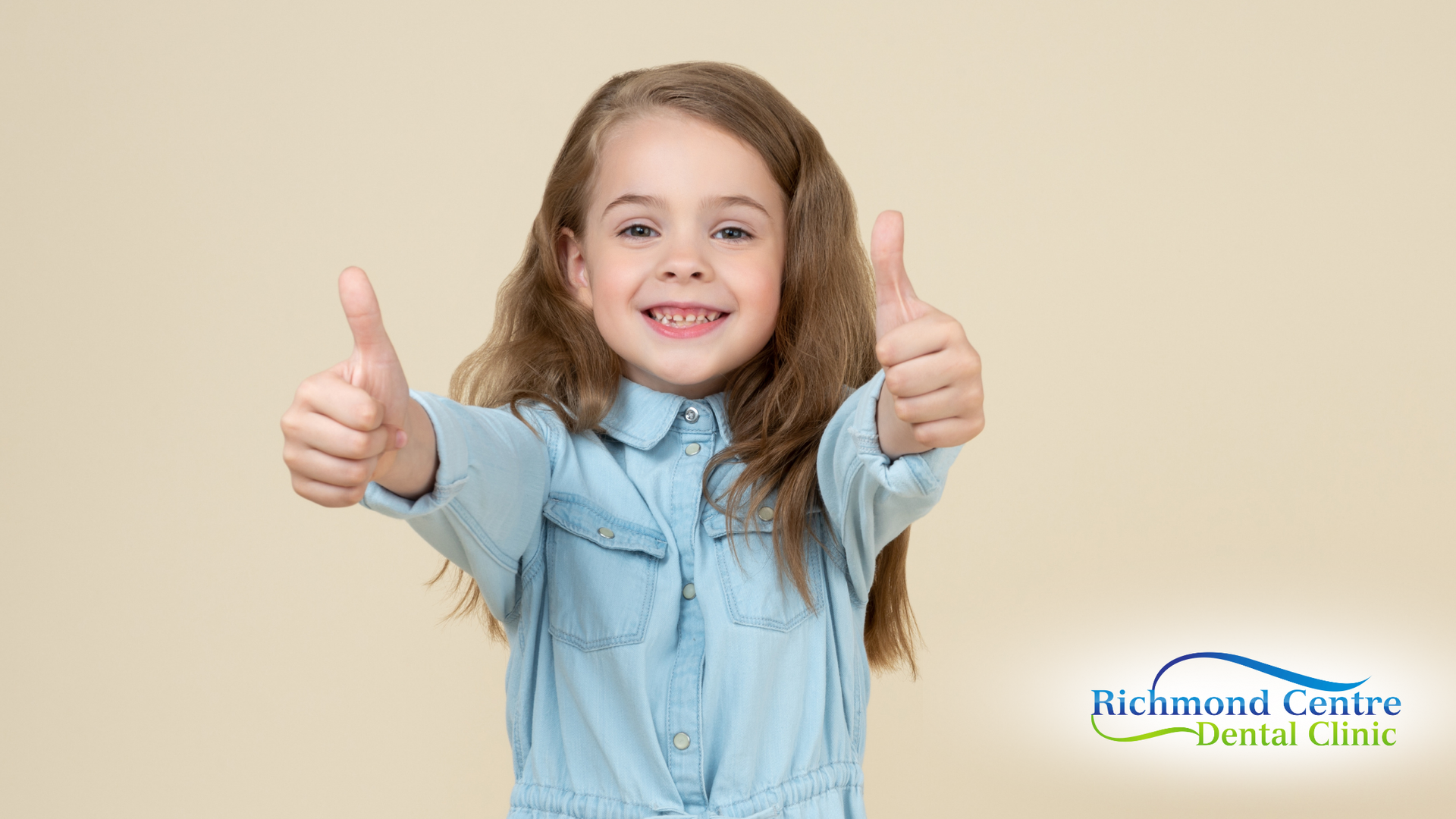 Girl with light brown hair in a blue shirt giving a double thumbs up, smiling. Beige background.