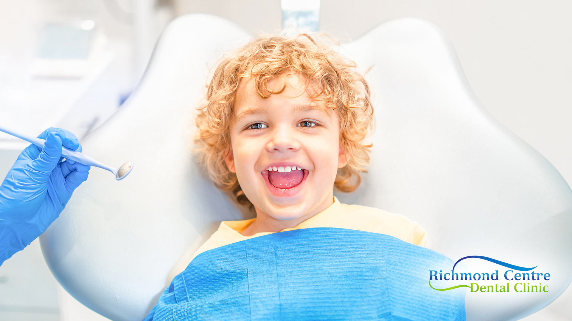 Smiling child in a dental chair with an open mouth, dental instruments, blue gloves.